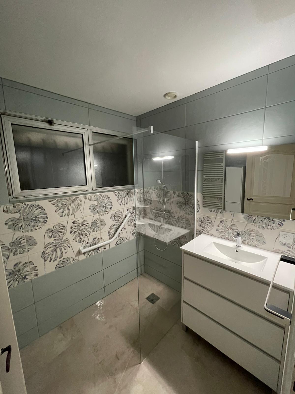 Salle de bain rénovée avec douche italienne et carrelage motif feuillage tropical