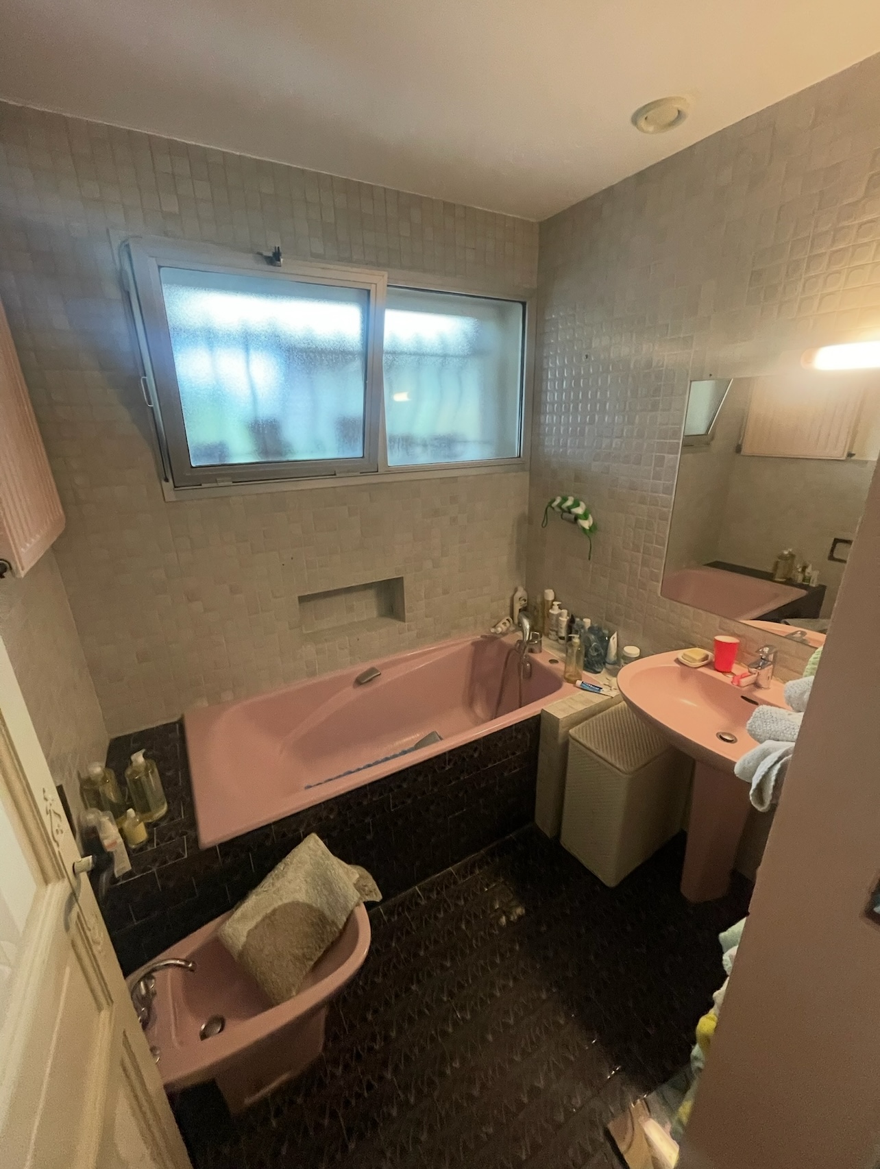 Salle de bain d'origine avec baignoire et sanitaires roses, carrelage daté